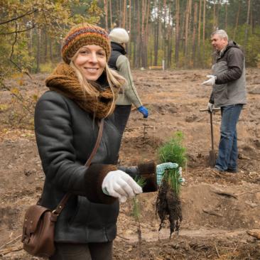 Uśmiechnięta, młoda kobieta w lesie, z rośliną w dłoni